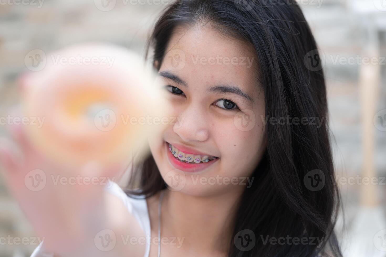 ritratto di asiatico donna mangiare ciambella nel il cucina a casa foto