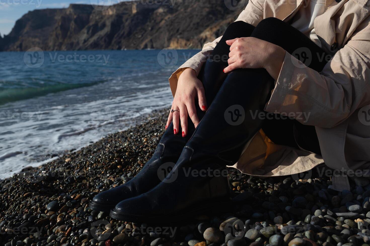 avvicinamento sparo. femmina mani abbracciare ginocchia seduta su il riva del mare foto