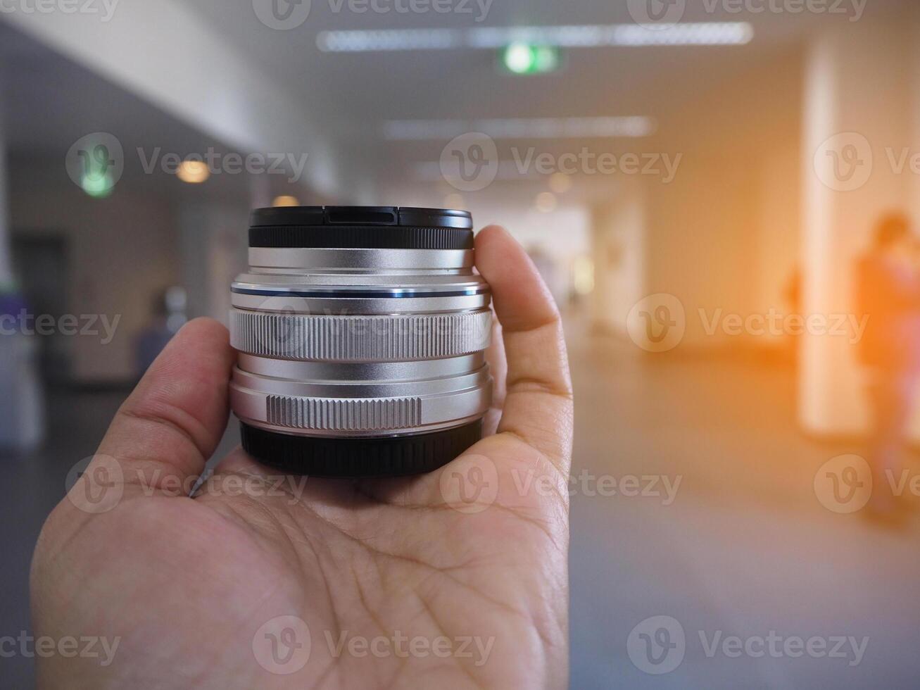 fotografo detiene un' telecamera lente nel sua mano nel edificio con luce del sole effetto. foto