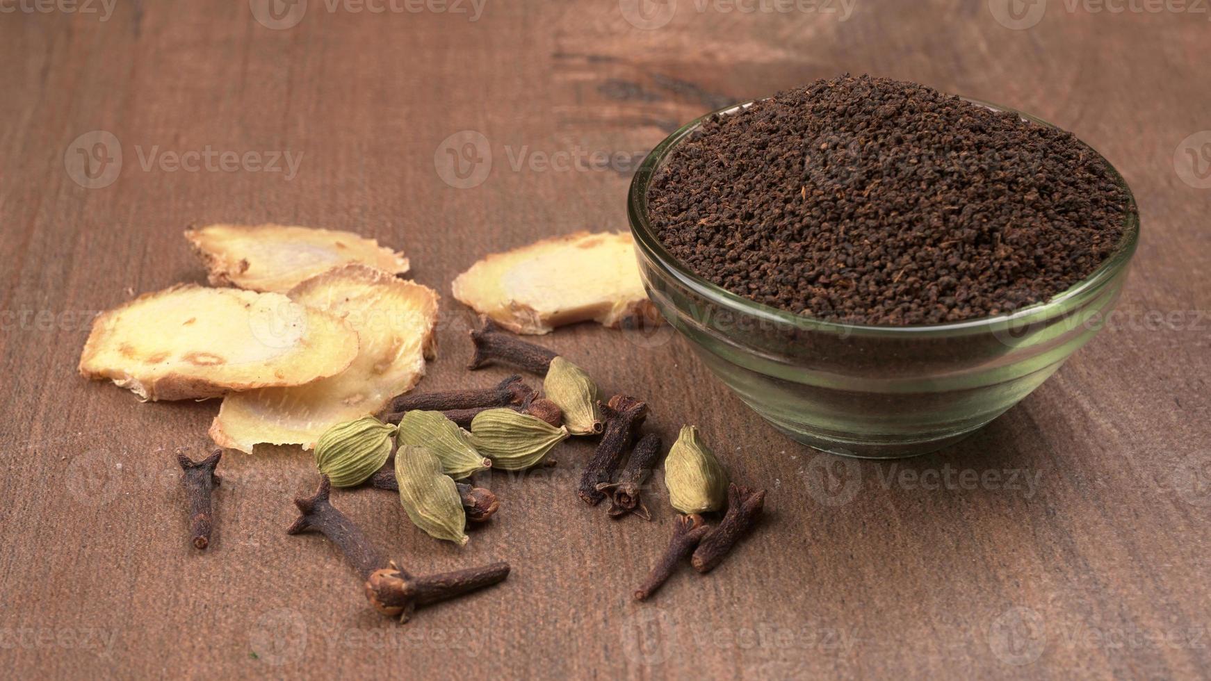 tè nero in polvere o polvere secca di tè in polvere, chai patti isolati in una ciotola di vetro con cardamomo, chiodi di garofano e zenzero. foto