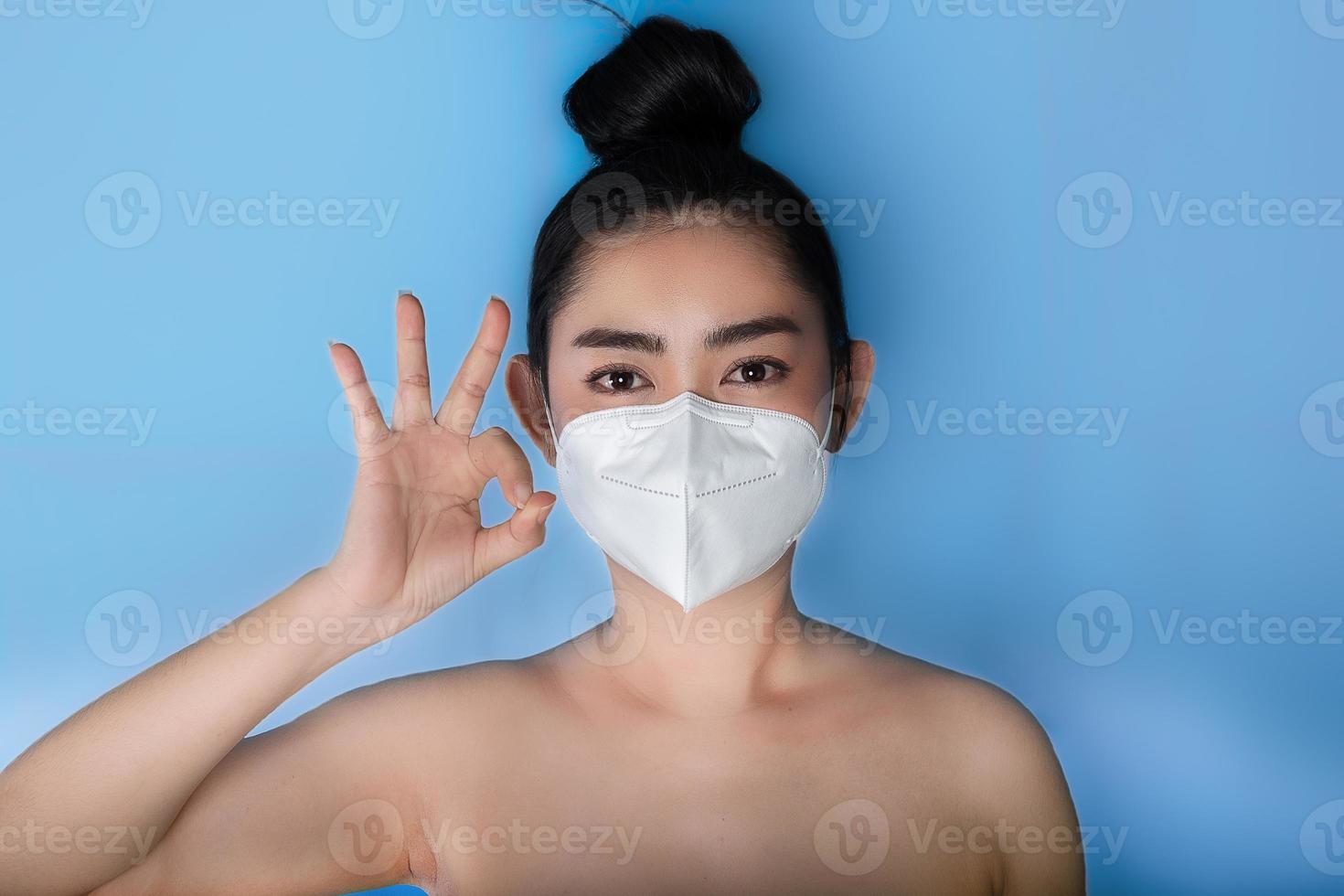 primo piano di una donna che indossa una maschera respiratore n95 per proteggersi dalle malattie respiratorie trasmesse dall'aria come l'influenza covid-19 corona pm2.5 polvere e smog, gesto femminile di pollice in su con la mano che mostra segno ok foto