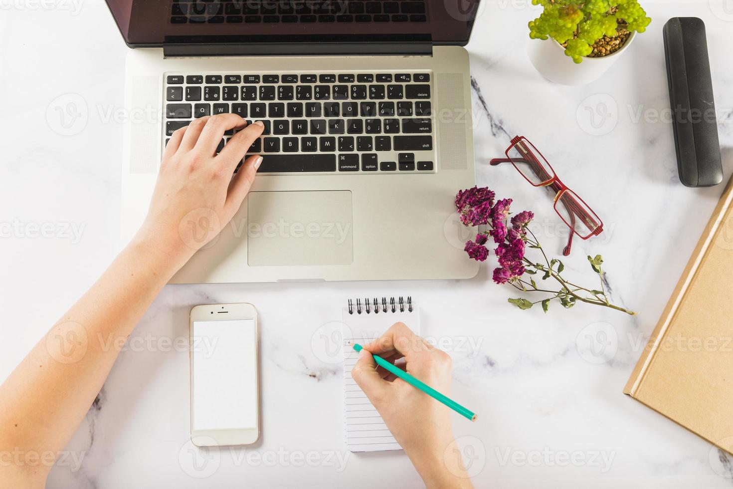 ritaglia le mani usando il laptop per prendere appunti sul tavolo di marmo foto