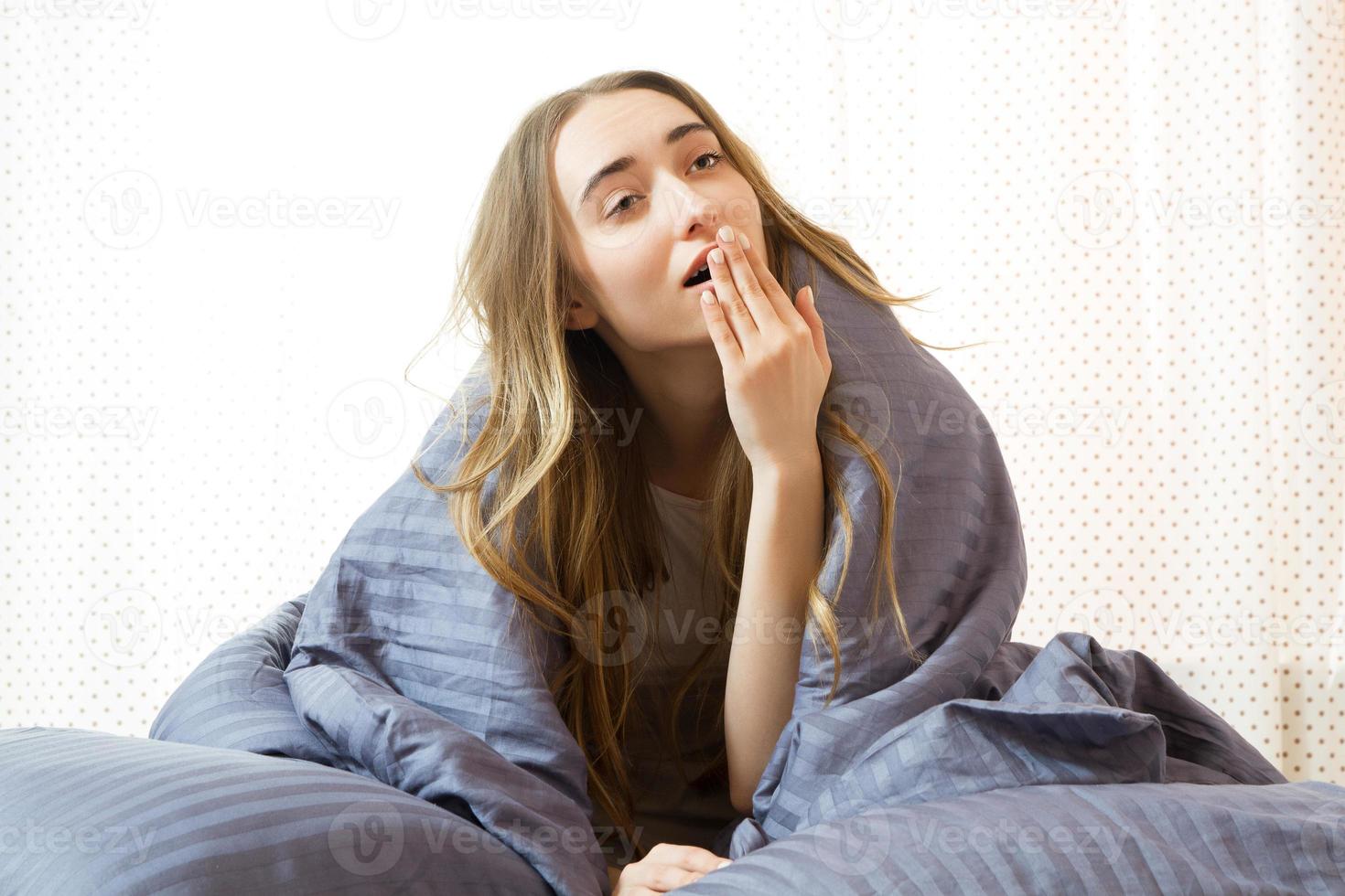 sbadigliando ragazza carina al mattino sotto le coperte sul letto - ha bisogno di andare al lavoro foto