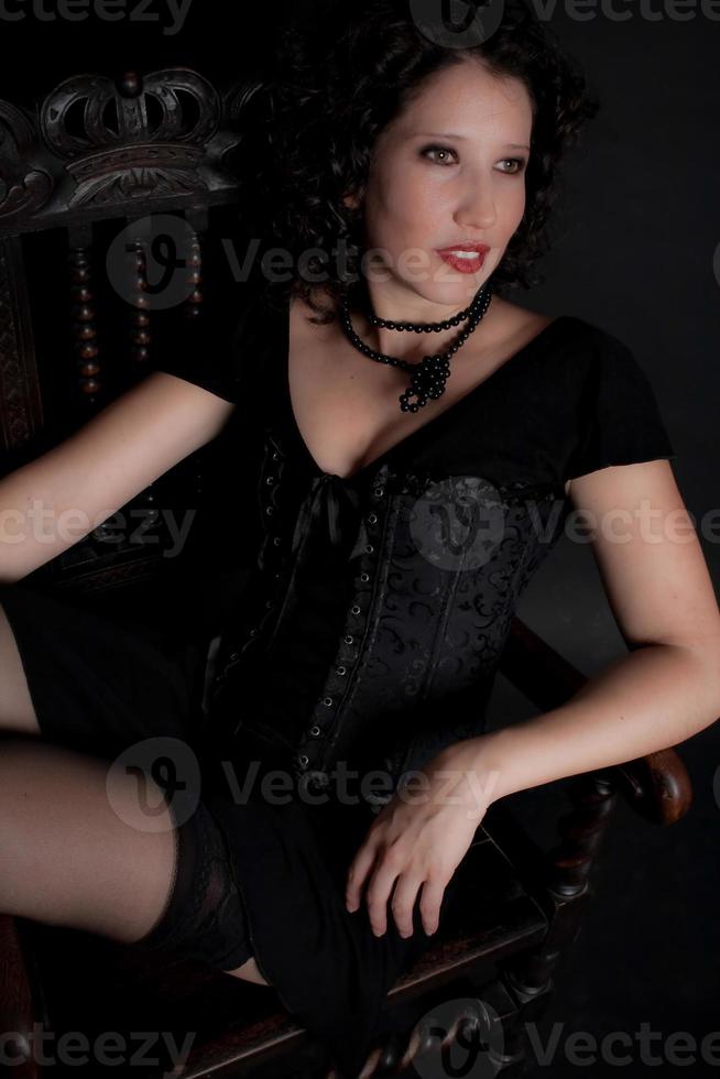 bella giovane donna dagli occhi verdi in corsetto nero con collana di pietra seduta di fronte al lato. foto