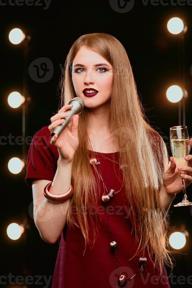 giovane smiley bei capelli lunghi in abito rosso donna con microfono cantando una canzone sul palco del karaoke foto