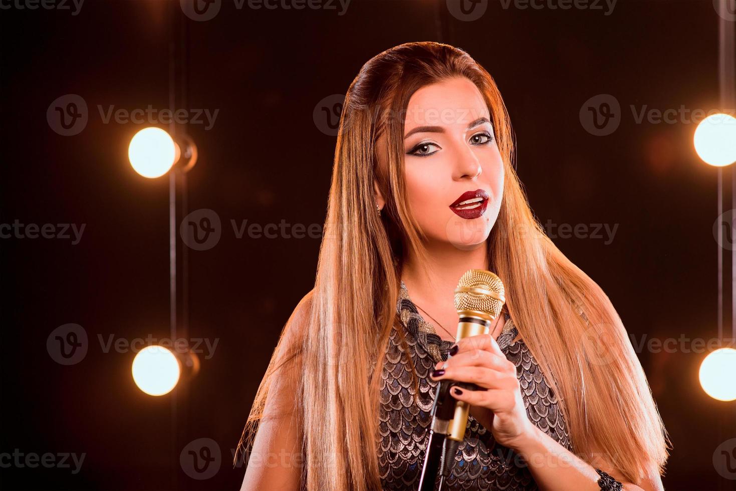 giovane faccina bella ragazza dai capelli lunghi con microfono che canta una canzone sul palco del karaoke foto