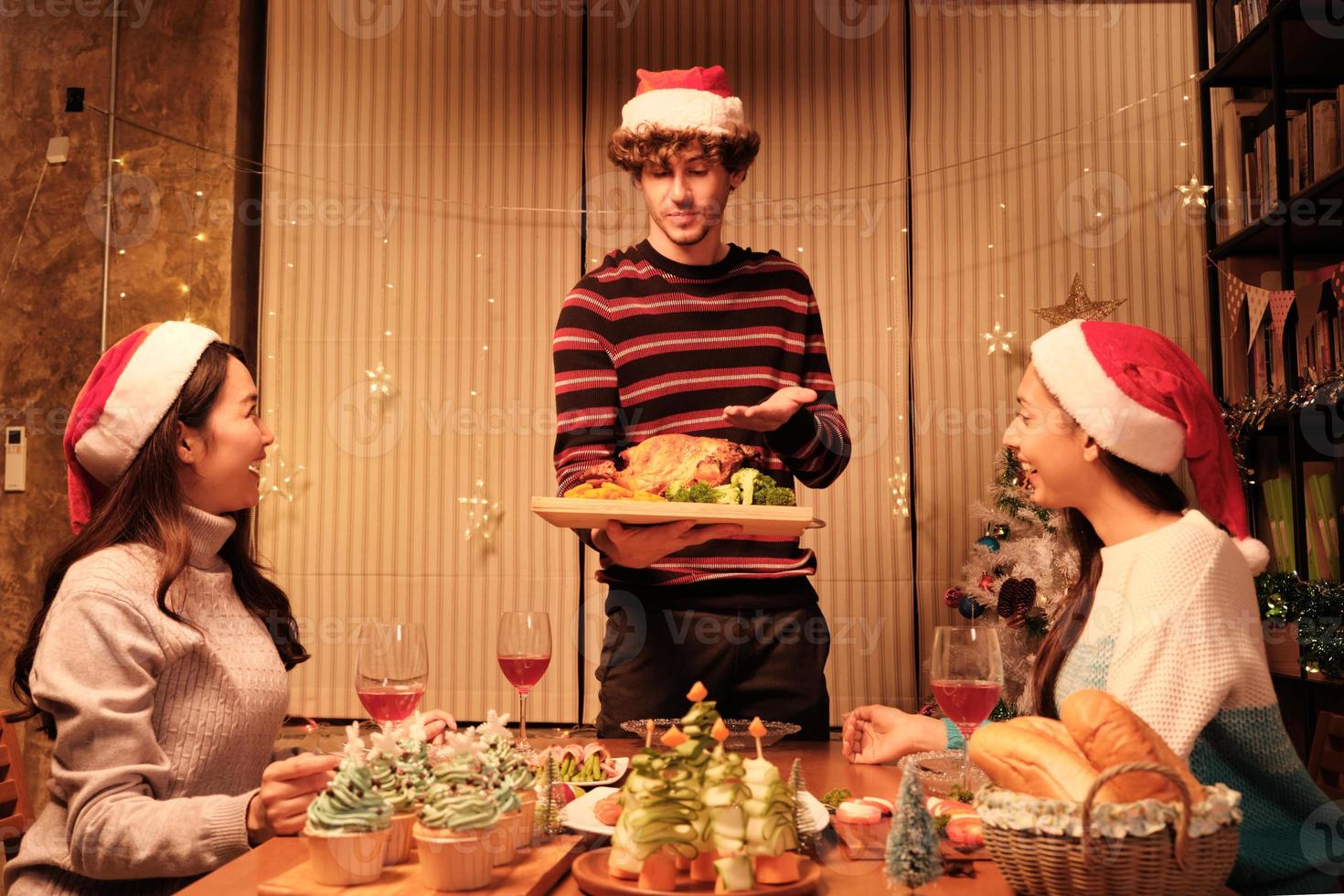 pasto speciale della famiglia, il giovane maschio serve tacchino arrosto agli amici, allegro con bevande e buon appetito, cena nella sala da pranzo di casa decorata per la festa di Natale e la festa di Capodanno. foto