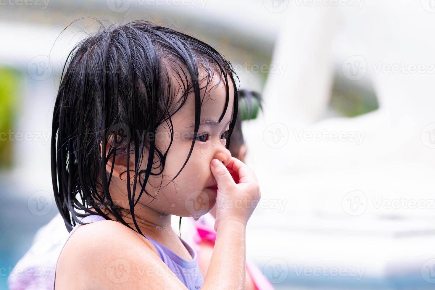 il primo piano del bambino sta schiacciando l'area del suo naso per espellere l'acqua dal suo naso. colpo alla testa della vista laterale di una bambina che gioca bagnata nella piscina blu del resort durante le vacanze. i bambini imparano a nuotare. foto