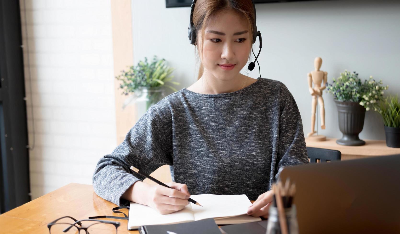 mano ravvicinata di una donna asiatica che studia online da casa prendendo appunti per l'apprendimento a distanza degli studenti sul laptop facendo i compiti, guardando la lezione video di ascolto. concetto di educazione a distanza. foto