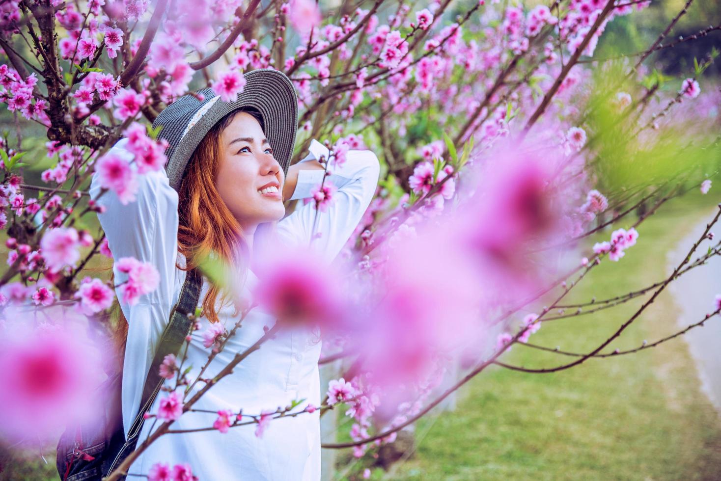 donna viaggiatrice con zaino che tiene il cappello viaggia per vedere i fiori di ciliegio rosa e godersi una natura bellissima. concetto di viaggio di voglia di viaggiare. foto