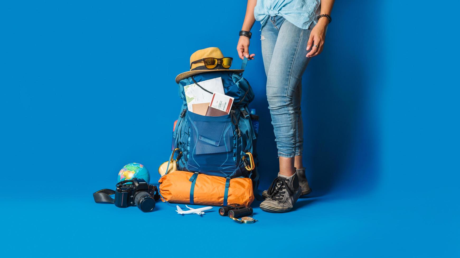 pianificazione turistica vacanza con l'aiuto della mappa del mondo con altri accessori da viaggio in giro. donna che viaggia con la valigia su sfondo di colore blu. zaino da viaggio concept foto