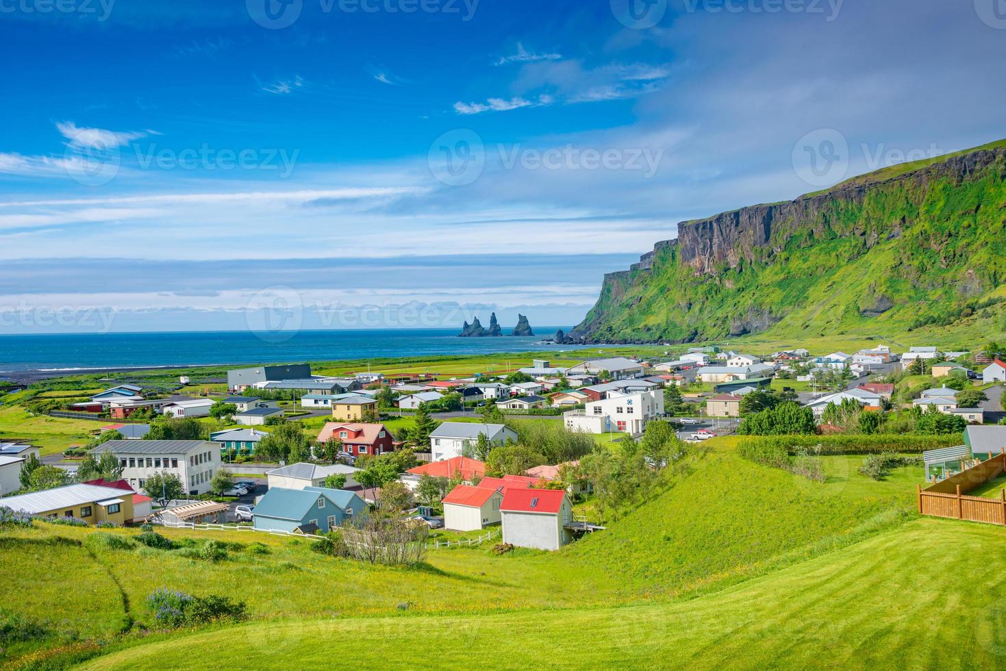 vista di pile di basalto reynisdrangar, spiaggia di sabbia nera vulcanica e lupino viola e fiori di prato gialli nella città di vik, nel sud dell'Islanda, in estate giornata di sole e cielo blu. foto