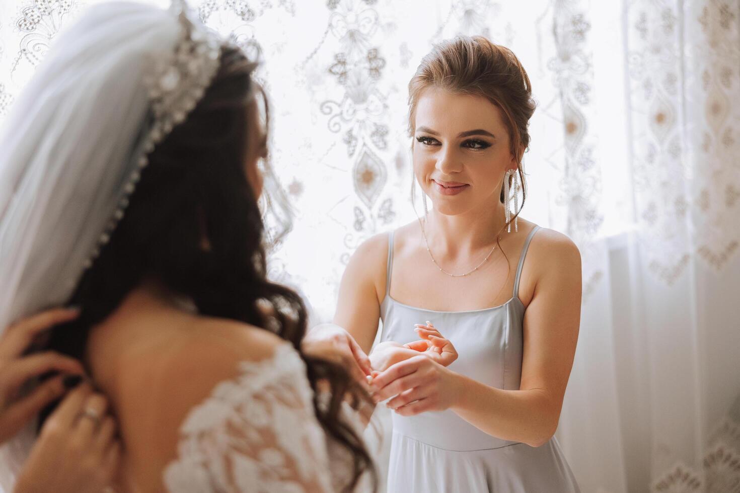 mattina di il sposa. il della sposa domestica di onore aiuta il sposa pizzo su sua vestire, allacciare pulsanti su il vestito o maniche. amiche Aiuto il sposa allacciare sua vestito foto