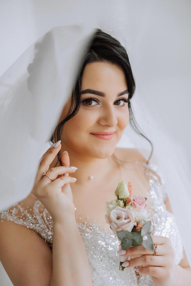 moda foto di un' bellissimo sposa con buio capelli nel un elegante nozze vestito e sbalorditivo trucco nel il camera su il mattina di il nozze. il sposa è preparazione per il nozze