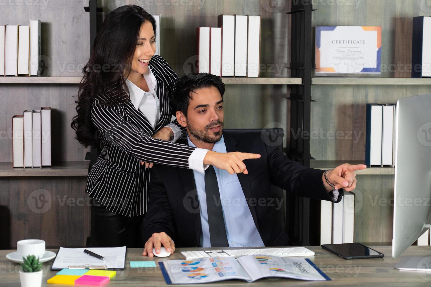 giovane uomo d'affari del Medio Oriente seduto su una sedia e imprenditrice caucasica in piedi accanto al suo collega in ufficio. concetto di business foto