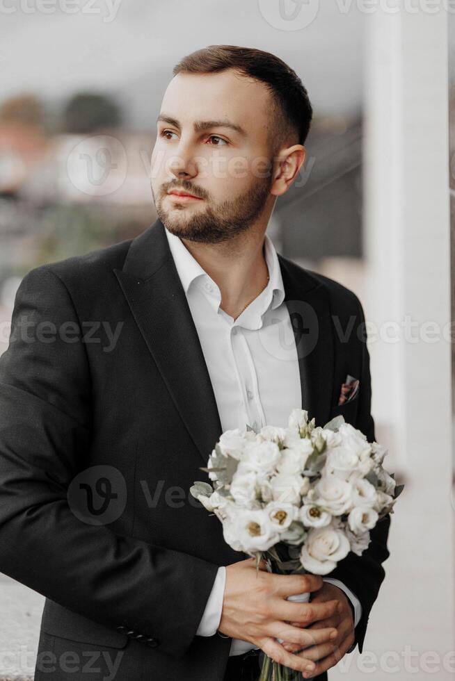 ritratto di un' bello uomo con fiori nel il suo mani su il balcone di un' Hotel camera nel il mattina. preparazione per un evento o un' nuovo Lavorando giorno. nuovo opportunità, conoscenti. avvicinamento ritratto foto