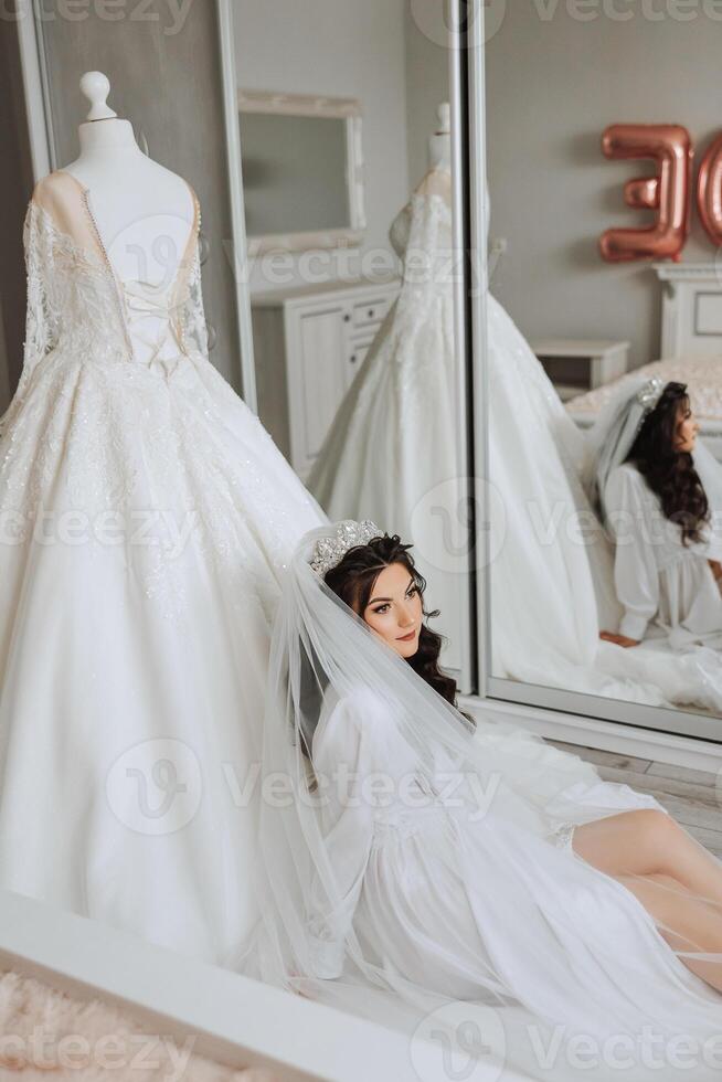 ritratto di un' lussuoso sposa nel boudoir stile vicino un' specchio con riflessione. preparazione il sposa per il nozze nel il mattina nel un' bianca veste. foto