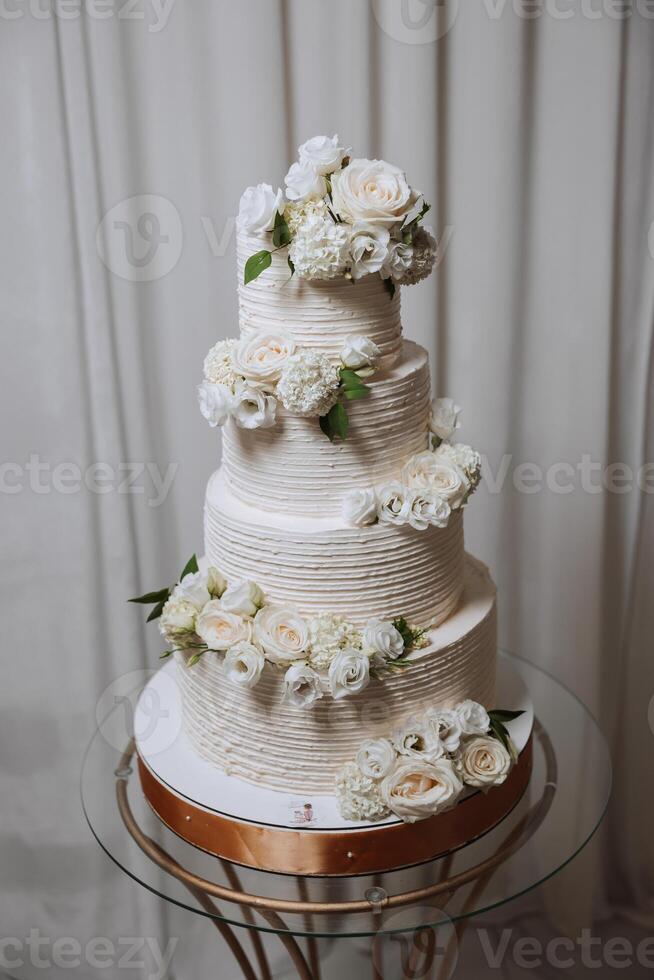 un' grande lussuoso multilivello nozze torta è decorato con fresco bianca rosa fiori nel il banchetto sala. nozze dolce sotto il sera luce. nozze arredamento. foto