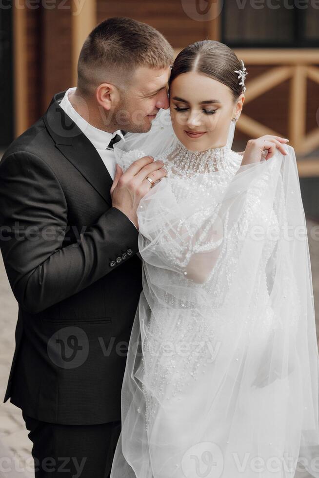 ritratto. un' sposa nel un elegante lungo vestito e velo e un' sposo nel un' completo da uomo posa mentre in piedi vicino alberi. nozze nel natura foto