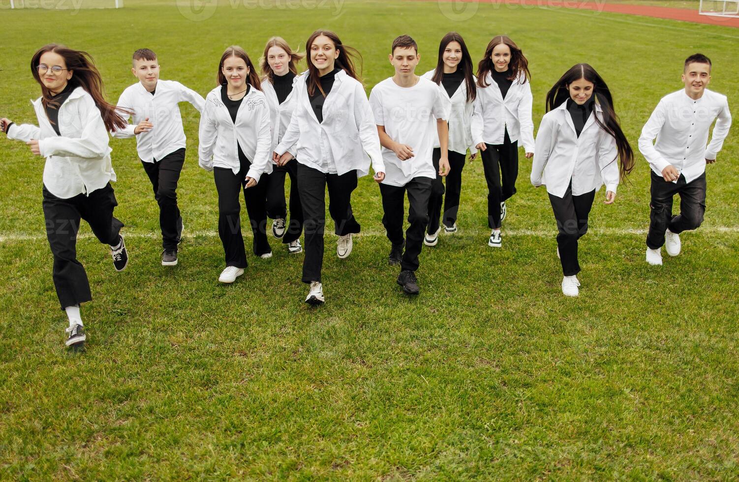 un' gruppo di molti contento adolescenti vestito nel il stesso attrezzatura avendo divertimento e in posa nel un' stadio vicino un' Università. concetto di amicizia, momenti di felicità. scuola amicizia foto