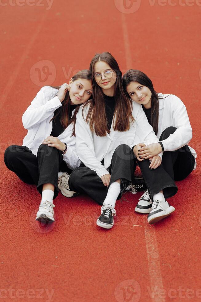 ritratto di tre adolescenziale ragazze nel casuale Abiti seduta nel un' stadio e in posa guardare a il telecamera. concetto di amicizia. un' momento di felicità. foto