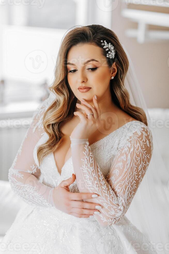 bellissimo sposa nel un' lussuoso nozze vestito con un' alla moda nozze acconciatura, professionale trucco. avvicinamento ritratto di giovane bellissima sposa nel camera a partire dal mattina. alto qualità foto. foto