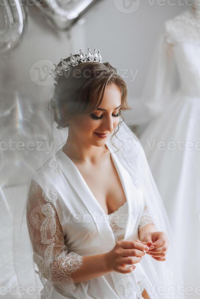 un' bellissimo brunetta sposa con un' tiara nel sua capelli è ottenere pronto per il nozze nel un' bellissimo accappatoio nel boudoir stile. avvicinamento nozze ritratto, foto. foto