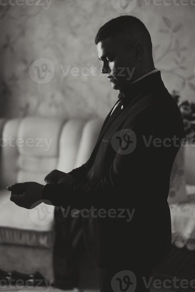 il sposo si allaccia il pulsante su il giacca di il quello dello sposo mattina incontri. preparazione il sposo per il nozze. nero e bianca foto. foto