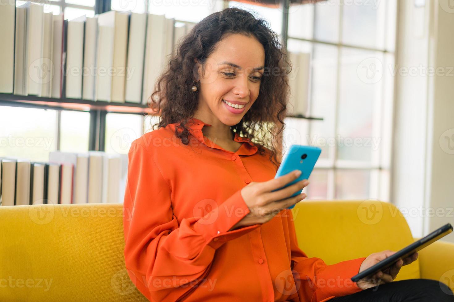 donna latina che utilizza il telefono cellulare o lo smartphone e tiene in mano un tablet foto