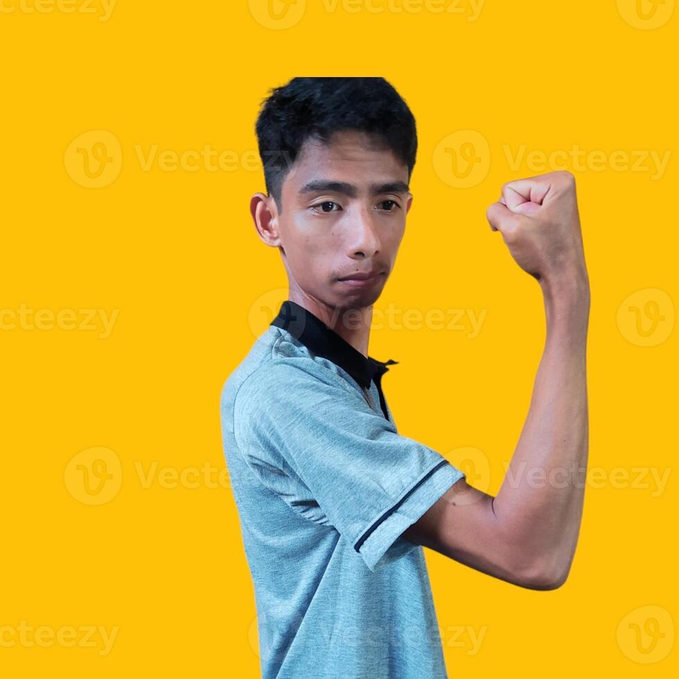 eccitato asiatico uomo indossare grigio maglietta mostrando forte movimento raccolta braccia, giallo sfondo. foto