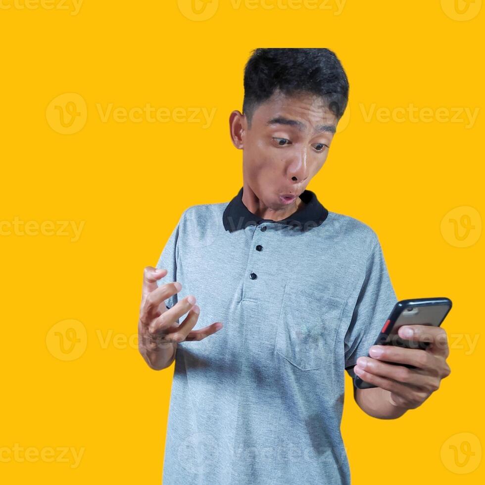eccitato giovane uomo Tenere un' inteligente Telefono indossare un' grigio maglietta, giallo sfondo. foto