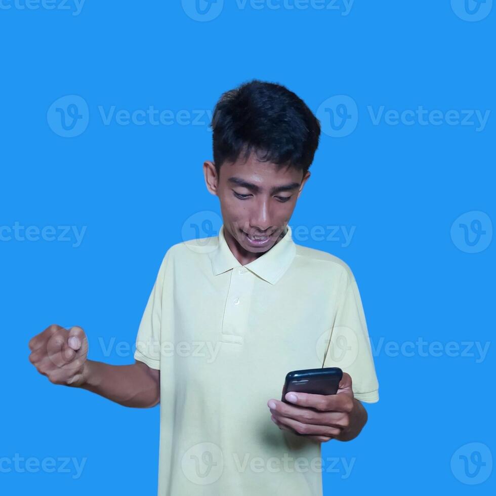 giovane asiatico uomo sorpreso guardare a inteligente Telefono isolato blu sfondo foto