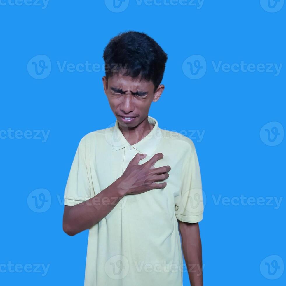 giovane asiatico uomo urgente il petto doloroso espressione, cuore attacco, crampi. isolato blu sfondo. foto