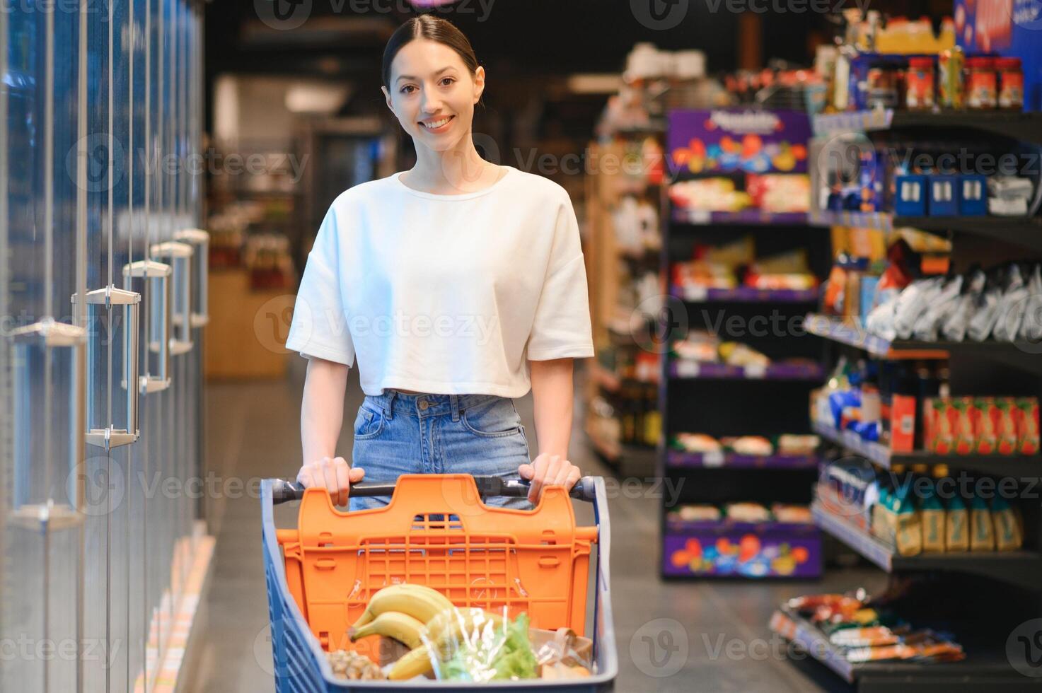 sorridente contento donna godendo shopping a il supermercato, lei è pendente su un' pieno carrello foto