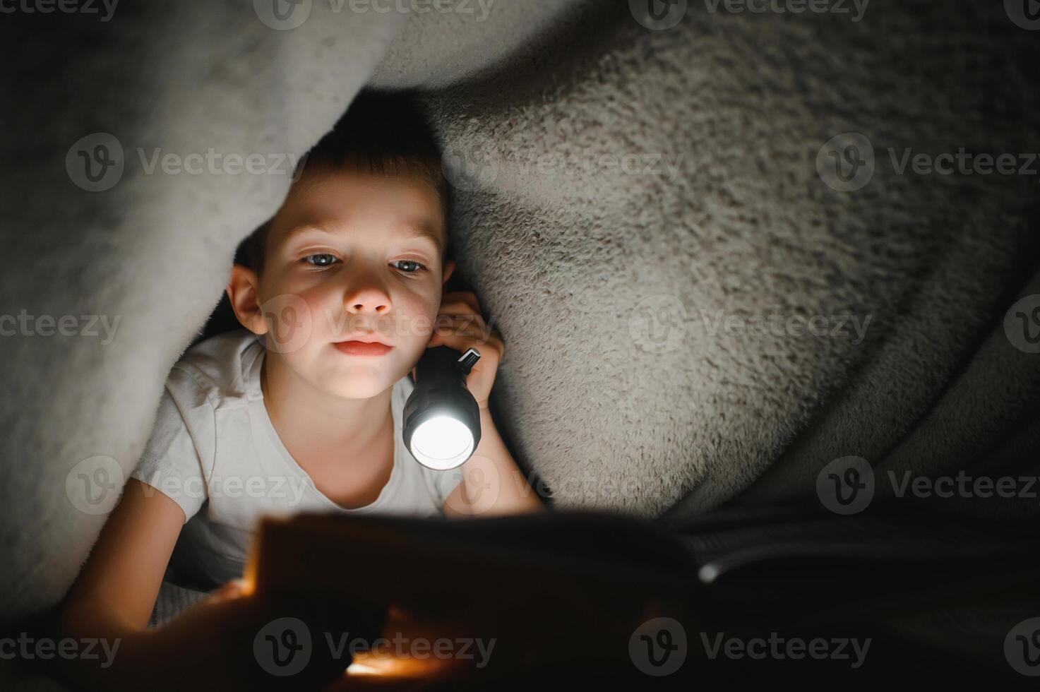 bambino lettura libro nel letto. bambini leggere a notte. poco ragazzo con Fata racconto libri nel Camera da letto . formazione scolastica per giovane bambini. di andare a dormire storia nel il sera. carino ragazzo sotto coperta nel buio camera con lampada foto