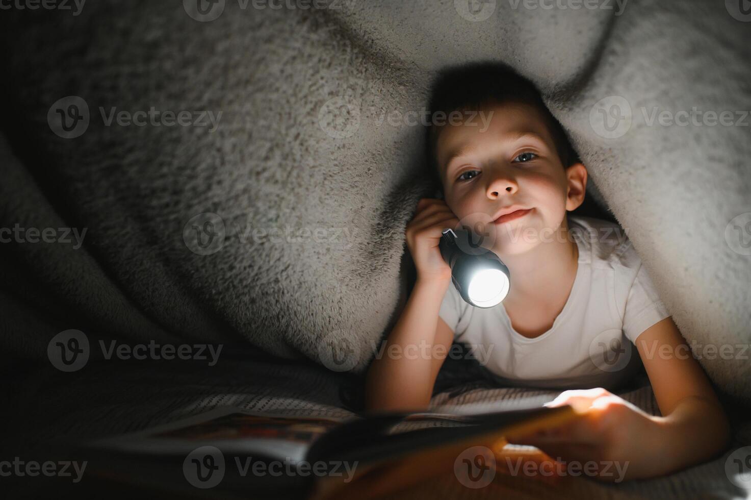 bambino lettura libro nel letto. bambini leggere a notte. poco ragazzo con Fata racconto libri nel Camera da letto . formazione scolastica per giovane bambini. di andare a dormire storia nel il sera. carino ragazzo sotto coperta nel buio camera con lampada foto