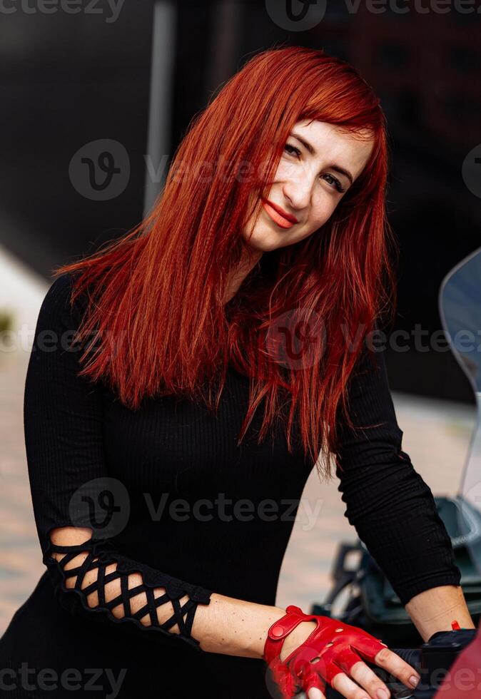 donna con rosso capelli seduta su un' motociclo. un' donna con ardente rosso capelli con fiducia si siede su un' motociclo, pronto per colpire il strada. foto