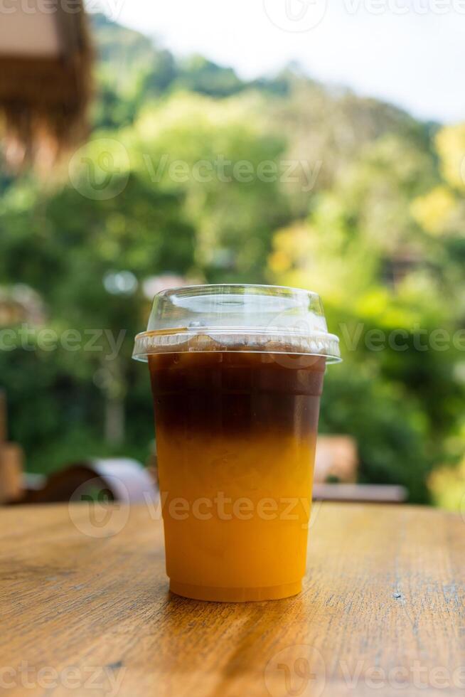 freddo nero caffè con fresco arancia succo, esso mostrando il struttura di Due strato e rinfrescante Guarda di il bevanda su legna tavolo. foto