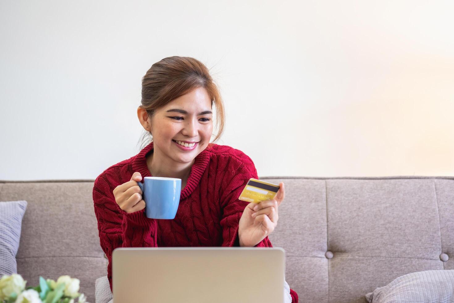 un' giovane asiatico donna con un' contento Sorridi detiene un' credito carta e usi un' smartphone per negozio in linea in linea pagamento concetto. foto