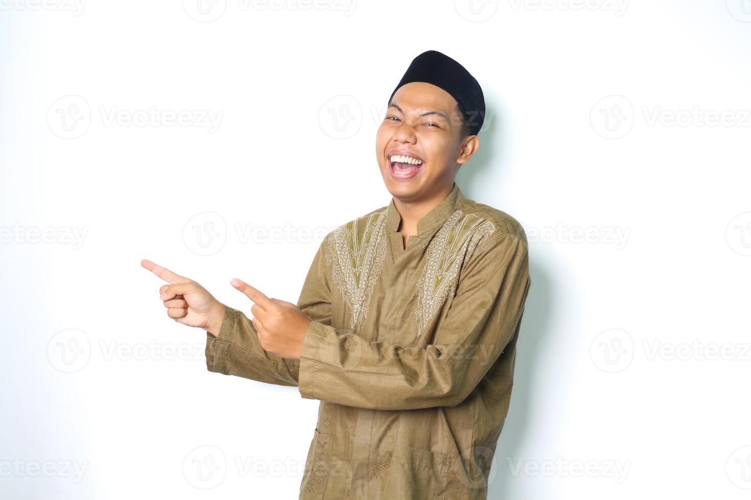 estatico asiatico musulmano uomo indossare islamico vestito puntamento per vuoto lato con ridere isolato su bianca sfondo foto