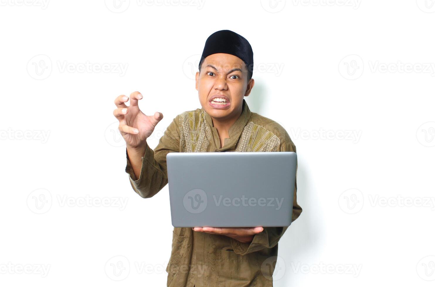 asiatico musulmano uomo Tenere il computer portatile con arrabbiato espressione indossare islamico vestito isolato su bianca sfondo foto