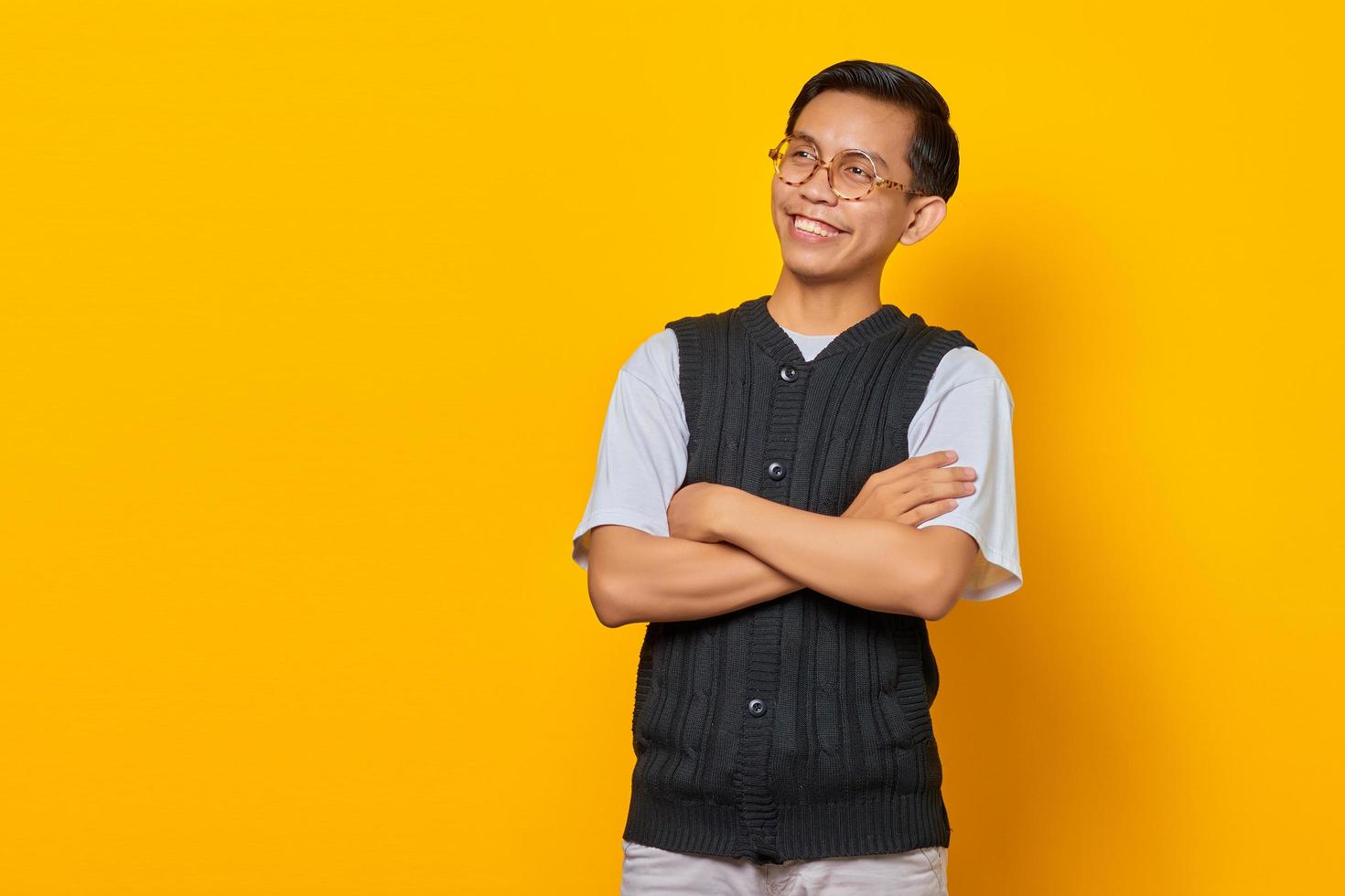 ritratto di sorridente giovane asiatico con le braccia incrociate isolato su sfondo giallo foto