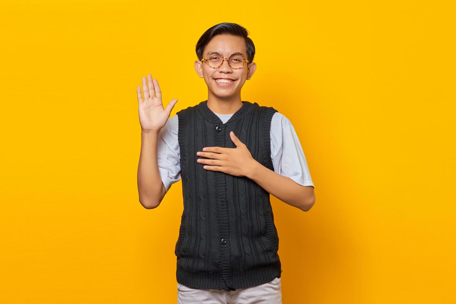 giovane asiatico sorridente e saluto isolato su sfondo giallo foto