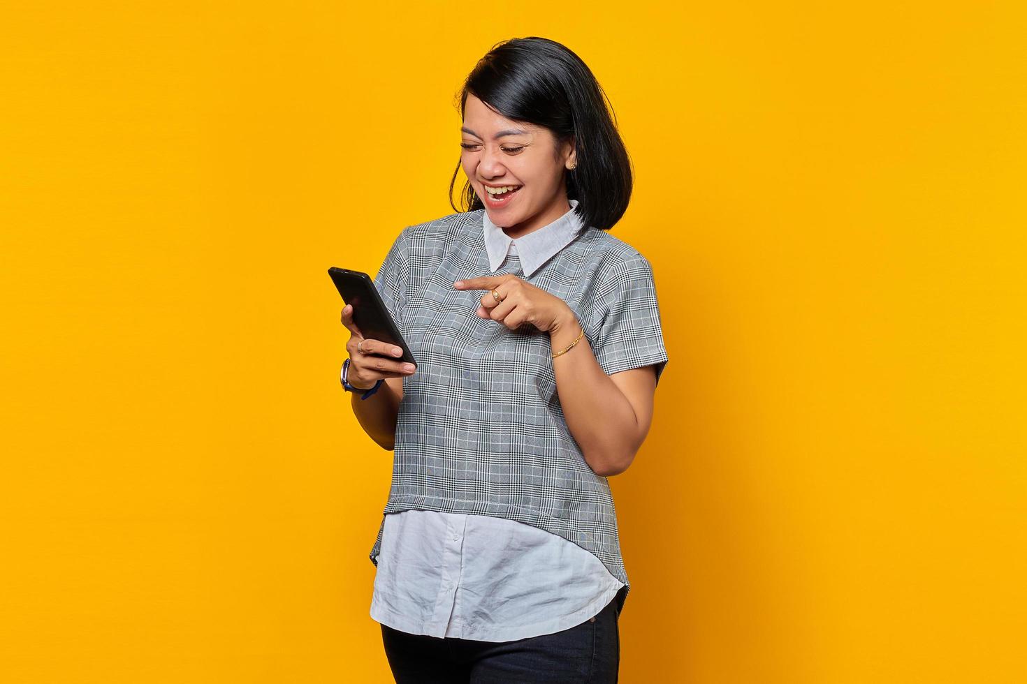 felice giovane donna asiatica che utilizza un telefono cellulare e guarda lo schermo dello smartphone su sfondo giallo foto