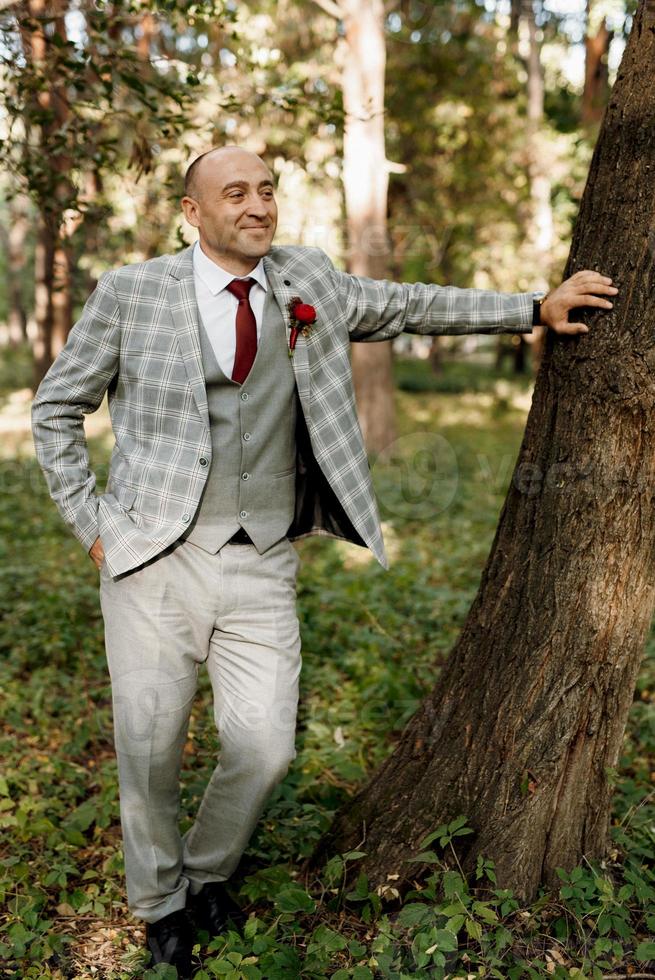 ragazzo calvo in una giacca grigia su uno sfondo di albero foto