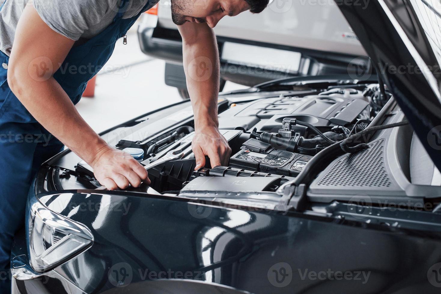 le mani del meccanico controllano la funzionalità dell'auto nel cofano aperto, primo piano. foto