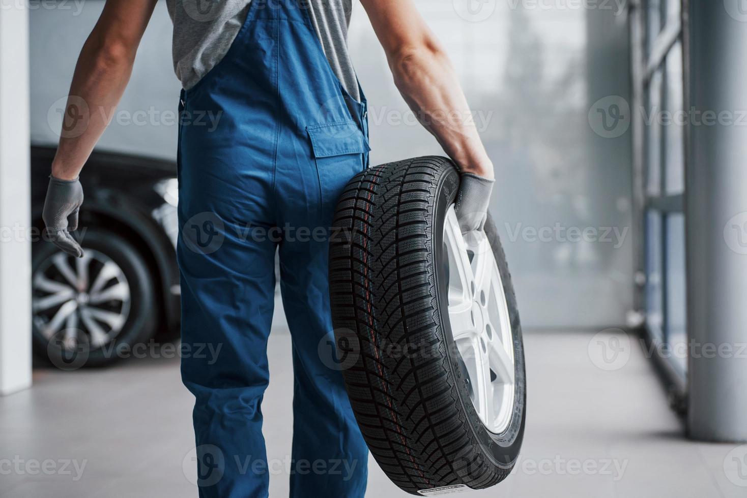 meccanico che tiene un pneumatico al garage di riparazione. sostituzione gomme invernali ed estive foto