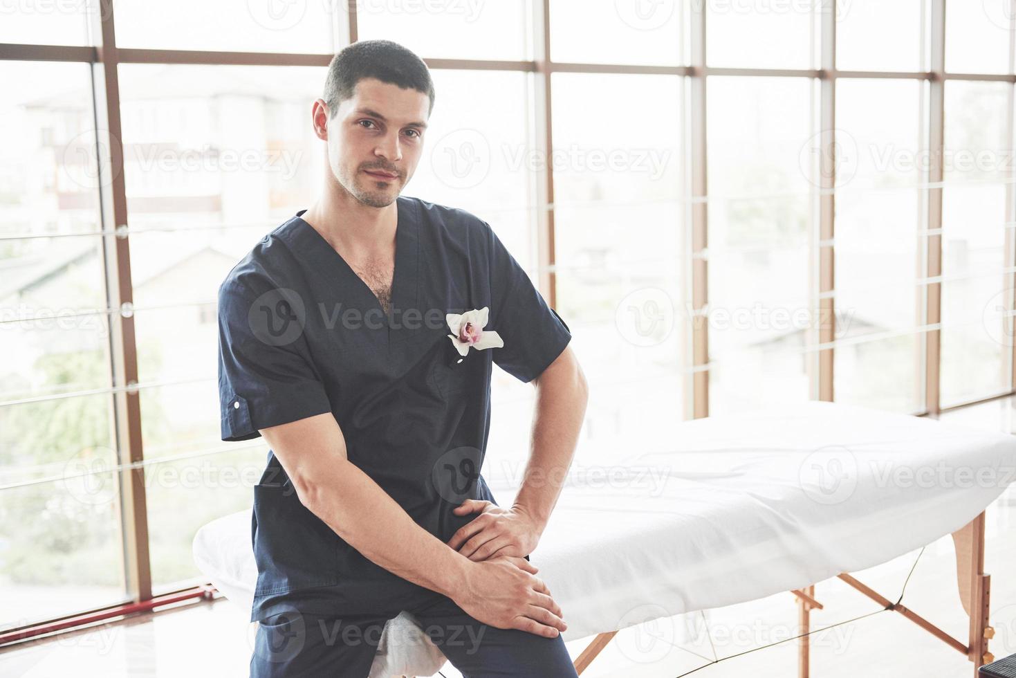 ritratto di giovane uomo sorridente in uniforme vicino a lettini da massaggio foto