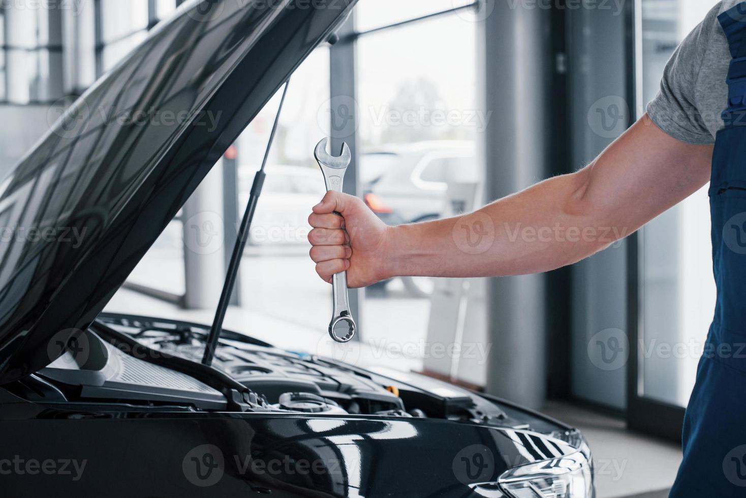 la mano di un meccanico con una chiave inglese in una zona combinata vicino all'auto in officina. foto