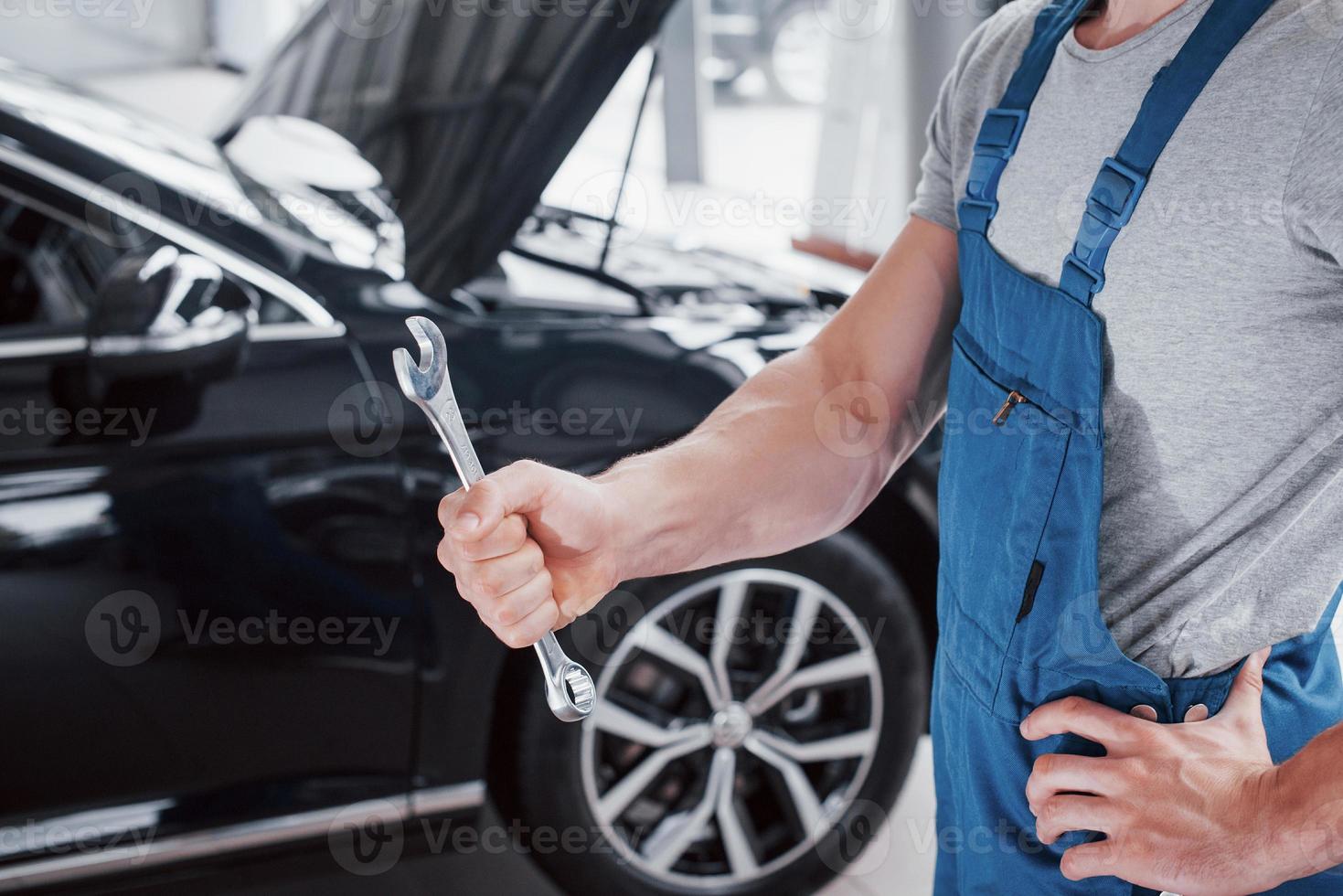 la mano di un meccanico con una chiave inglese in una zona combinata vicino all'auto in officina. foto